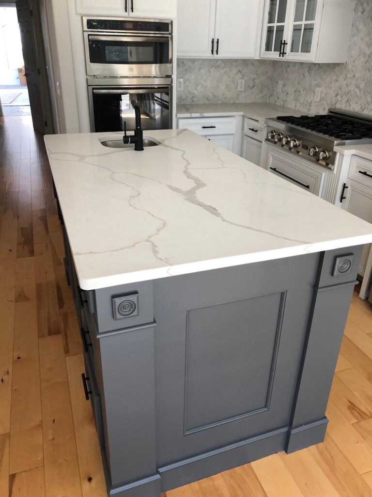 Modern kitchen island with white marble countertop, gray cabinets, and stainless steel appliances. Services.