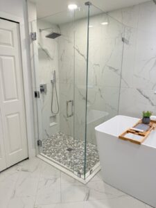 Modern bathroom featuring a frameless glass shower with marble tile and pebble floor, alongside a freestanding bathtub.