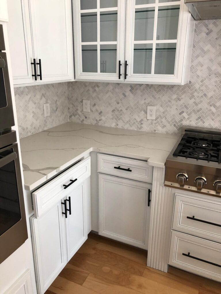 Services: Modern white kitchen design with custom cabinets, sleek black hardware, quartz countertops, and herringbone backsplash.