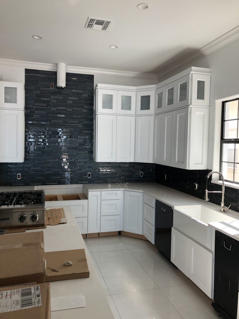 Modern kitchen renovation with white cabinets, dark backsplash, farmhouse sink, and stainless steel appliances. Home interior design.