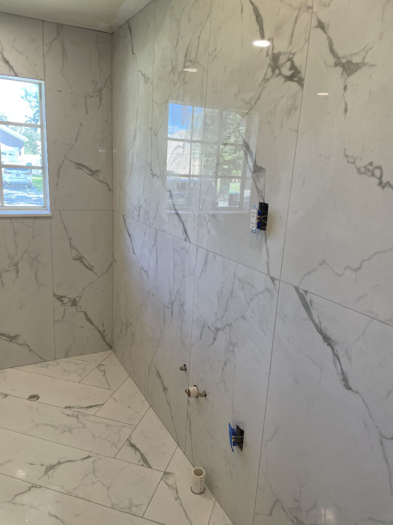 Modern bathroom remodel featuring white marble-look tile on walls and floor, showcasing elegant design and bright interior.